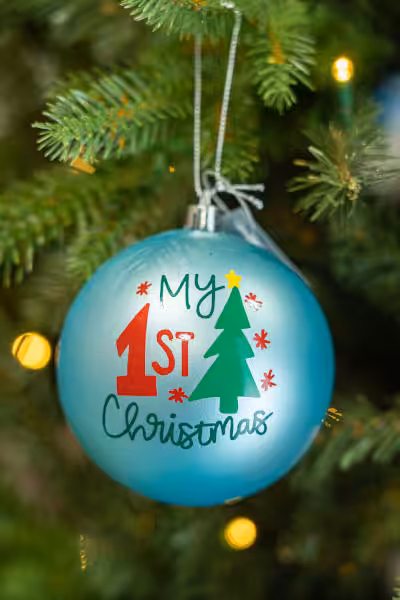 teal coloured custom christmas bulb with words my 1st christmas beside a christmas tree caricature