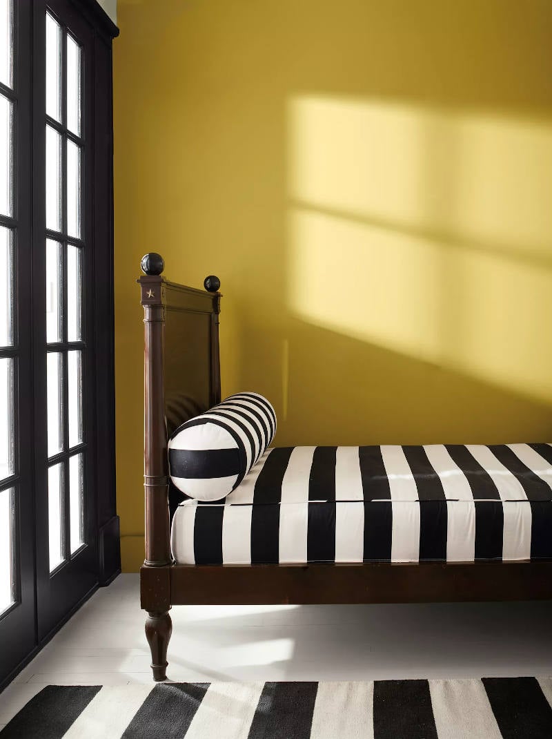 bed made up in black and white stripes with walls painted savannah green