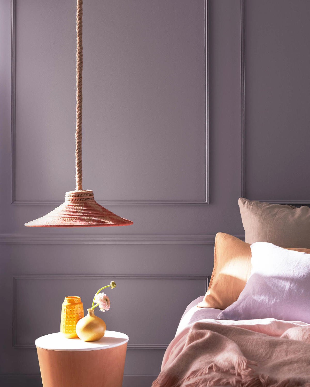 wall painted with benjamin moore hazy lilac colour in a room with a bed, small table, and lamp.